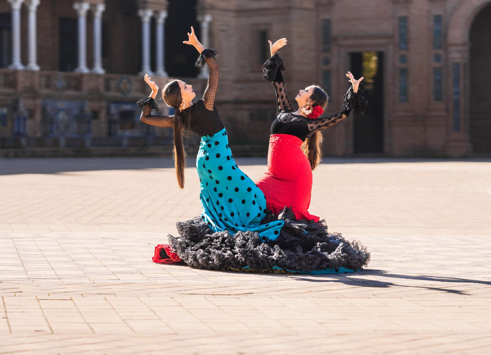 Two Women Dressed In Flamenco Costume Doing A Choreography In A Square
